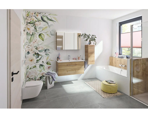 Modernes, helles Badezimmer mit Waschtischunterschrank in Holzoptik, Spiegelschrank, weißer Badewanne und floraler Wandgestaltung.