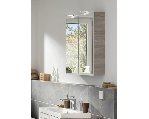 Modernes Badezimmer mit zweitürigem Spiegelschrank inklusive LED-Beleuchtung und grauer Holzoptik, weißem Waschbecken und verchromter Armatur.