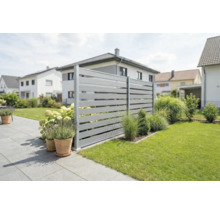 Moderner Sichtschutzzaun aus grauen horizontalen Lamellen in einem gepflegten Garten mit Terrasse, Rasen und Pflanzgefäßen.