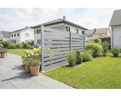 Moderner Sichtschutzzaun aus grauen horizontalen Lamellen in einem gepflegten Garten mit Terrasse, Rasen und Pflanzgefäßen.