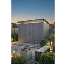 Modernes Gartenhaus mit Pultdach und Oberlichtern in einem Garten mit Steinplatten, Kies, Pflanzen und Außenbeleuchtung in der Dämmerung.