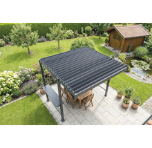 Freistehende Pergola mit Lamellendach auf einer hellen Terrasse im Garten, inklusive Holzmöbeln, angrenzendem Teich und Gartenhaus im Hintergrund.