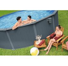 Ovaler Aufstellpool mit dunkelgrauer Lattenverkleidung im Garten. Ein Mann und ein Kind sind im Wasser, eine Frau sitzt daneben.