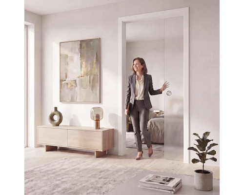 Moderne Glasschiebetür in hellem Innenraum, rahmenloses Design mit rundem Muschelgriff, Frau geht durch die geöffnete Tür.