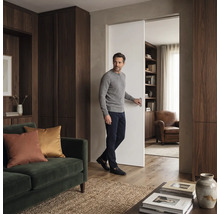 Ein Mann öffnet eine Schiebetür in einem Wohnraum mit Holzschränken, einem Sofa und angrenzendem Lesezimmer.