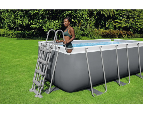 Rechteckiger Aufstellpool mit grauem Rahmen und weißem Rand, inklusive Sicherheitsleiter, auf einer Rasenfläche im Garten.