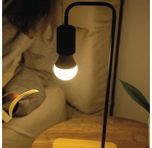 Moderne Tischleuchte mit minimalistischem Metallgestell und leuchtender LED-Lampe in einer Lesesituation.