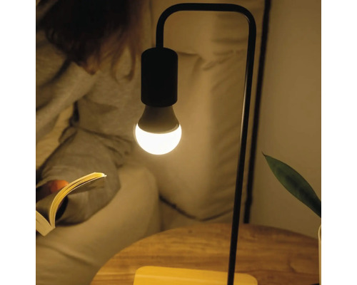 Moderne Tischleuchte mit minimalistischem Metallgestell und leuchtender LED-Lampe in einer Lesesituation.