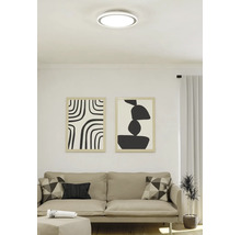 Moderne LED-Deckenleuchte in runder, flacher Form in einem hellen Wohnzimmer über einem Sofa.