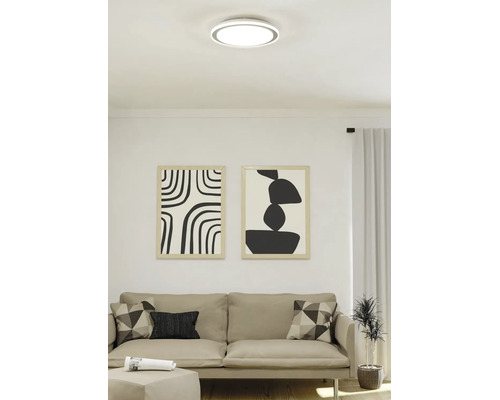 Moderne LED-Deckenleuchte in runder, flacher Form in einem hellen Wohnzimmer über einem Sofa.