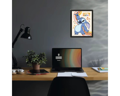Gerahmtes Poster mit Disney-Figur Stitch und Schriftzug Let's Dance über einem Schreibtisch mit Laptop und Lampe in einem modernen Arbeitszimmer.