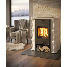 Kaminofen mit Keramikkacheln und brennendem Feuer in hellem Wohnzimmer mit Sessel, Decke und Teppich.