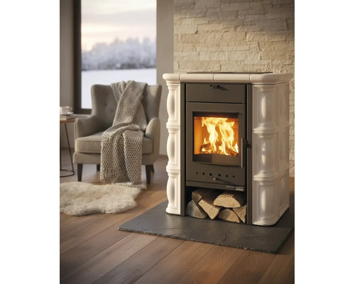 Kaminofen mit Keramikkacheln und brennendem Feuer in hellem Wohnzimmer mit Sessel, Decke und Teppich.