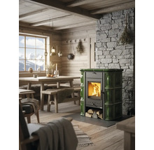 Grüner Kachelofen mit brennendem Holz in einer rustikalen Stube mit Steinwand und Holzmöbeln.