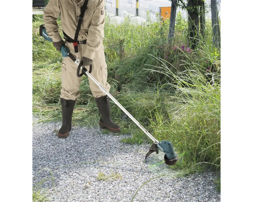Person bei Gartenarbeiten mit einer Makita Akku-Motorsense an einem Wegrand mit hohem Gras.