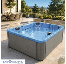 Eckiger Außenwhirlpool auf einer hellen Terrasse mit grauer Verkleidung und blauem Becken. Im Hintergrund Gartenmöbel und Bäume. Sanotechnik Logo.
