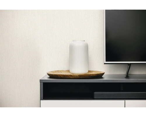 Hellbeige Vliestapete mit feiner Leinenstruktur in einem modernen Wohnzimmer hinter einem TV-Lowboard mit Dekoration.