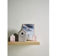 Dekorative Anordnung auf hellem Holzregal mit grauem Beton-Vogelhaus und hausförmigen Figuren in Rosa und Grau im minimalistischen Design.