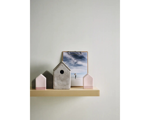 Dekorative Anordnung auf hellem Holzregal mit grauem Beton-Vogelhaus und hausförmigen Figuren in Rosa und Grau im minimalistischen Design.