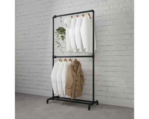 Schwarzer Kleiderständer aus Industrierohren mit zwei Ebenen, bestückt mit weißen Hemden, einem beigen Mantel und einer Hängepflanze.