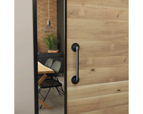 Schiebetür aus Holz mit schwarzem Stangengriff im Industrial-Design, Blick in ein Esszimmer mit Holztisch und schwarzen Stühlen.