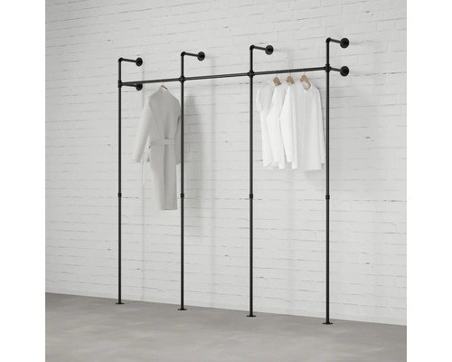 Industrielles Kleiderstangen-System aus schwarzen Metallrohren, Wand- und Bodenmontage, dreiteilig, mit hängender Kleidung vor einer Ziegelwand.
