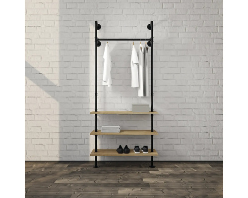 Offene Garderobe im Industrial-Stil aus schwarzen Metallrohren mit Kleiderstange und drei Holzregalen vor einer Ziegelwand.
