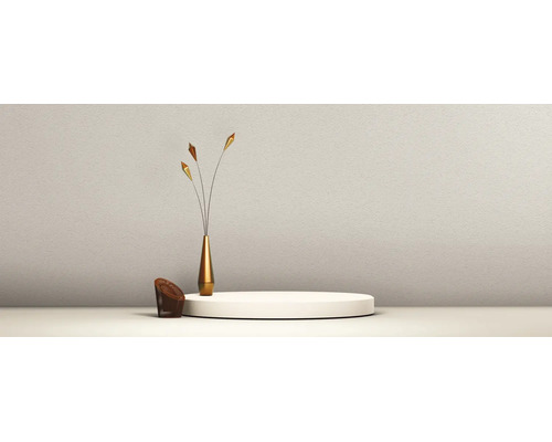 Minimalistische Szene mit einem weißen runden Podium, einer schlanken goldfarbenen Vase mit Dekozweigen und einem kleinen braunen Gittersessel vor einer strukturierten Wand.