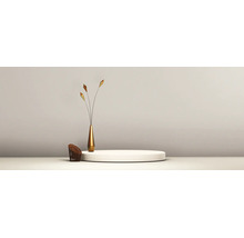 Minimalistische Einrichtung mit einem runden weißen Podest, einer schlanken goldenen Vase mit Dekostielen und einem kleinen geflochtenen Element.