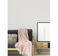 Helles, organisiertes Wohnzimmer mit strukturierter Wand, einem Sofa mit Fellkissen und Fransendecke sowie einem Beistelltisch aus Holz mit Poster.