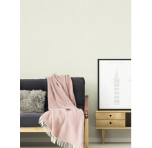 Hell gestrichene Wand in einem Wohnzimmer mit einem dunklen Sofa, einer rosa Wolldecke mit Fransen und einem Holz-Sideboard mit einem London-Poster.