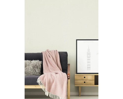 Hell gestrichene Wand in einem Wohnzimmer mit einem dunklen Sofa, einer rosa Wolldecke mit Fransen und einem Holz-Sideboard mit einem London-Poster.