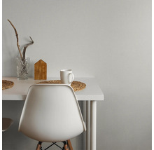 Moderner Arbeitsplatz mit weißem Schreibtisch und Stuhl vor einer grauen Wand mit Struktur. Dekoriert mit Glasvase, Holzhaus und Tasse.
