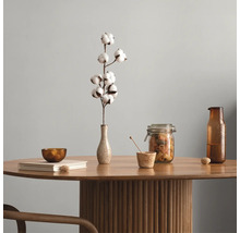 Runder Holztisch mit geriffeltem Säulenfuß, dekoriert mit einer Vase mit Baumwollzweig, einem Vorratsglas, einer Glasflasche und einem Buch.