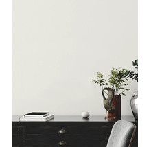 Helle minimalistische Szene mit einer hell gestrichenen Wand, einem dunklen Holzschreibtisch mit Dekoration, Büchern und einer Pflanze in einer Vase.