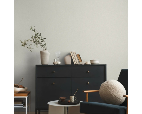 Helle Vliestapete mit feiner Struktur hinter einer dunklen Kommode in einem modern eingerichteten Wohnzimmer.