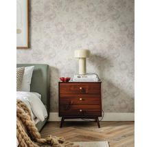 Dezent gemusterte Blumentapete mit großen Rosenmotiven im Schlafzimmer mit dunkler Holzkommode, cremefarbener Lampe und grünem Bettkopfteil.