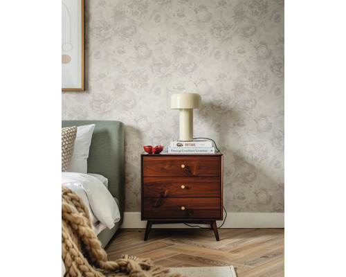 Dezent gemusterte Blumentapete mit großen Rosenmotiven im Schlafzimmer mit dunkler Holzkommode, cremefarbener Lampe und grünem Bettkopfteil.