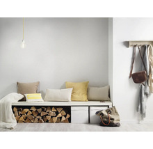 Heller minimalistischer Eingangsbereich mit weißer Bank, verschiedenen Kissen, Brennholzlager, zwei weißen Boxen und einer hölzernen Garderobe.