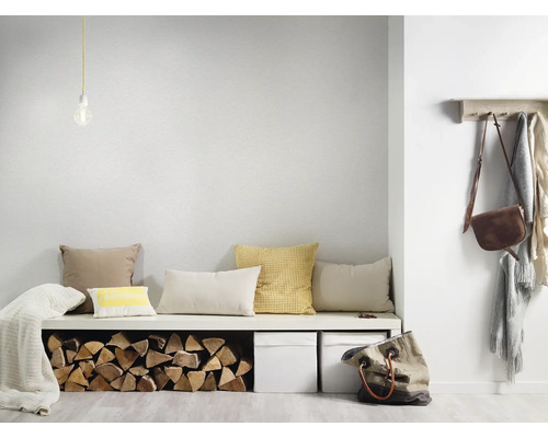 Heller minimalistischer Eingangsbereich mit weißer Bank, verschiedenen Kissen, Brennholzlager, zwei weißen Boxen und einer hölzernen Garderobe.