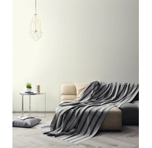Helles Wohnzimmer mit cremefarbener Wand, Sofa mit gestreifter Decke, Beistelltisch und geometrischer Pendelleuchte auf Parkettboden.