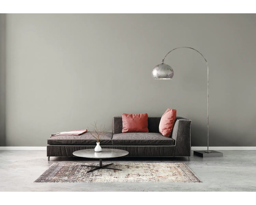 Modernes Wohnzimmer mit dunklem Sofa, Bogenstehleuchte, rundem Couchtisch und gemustertem Teppich vor einer grauen Wand.
