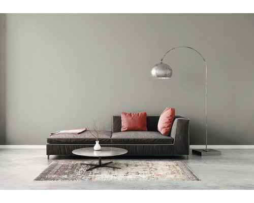 Modernes Wohnzimmer mit grauer Wand, dunkelgrauem Sofa, roten Kissen, silberner Bogenlampe und rundem Couchtisch auf einem gemusterten Teppich.