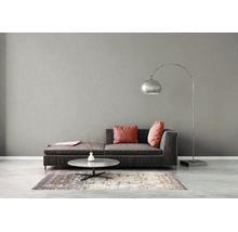 Modernes Wohnzimmer mit dunklem Sofa, rosa Kissen, rundem Steincouchtisch, silberner Bogenlampe und gemustertem Teppich vor grauer Wand.