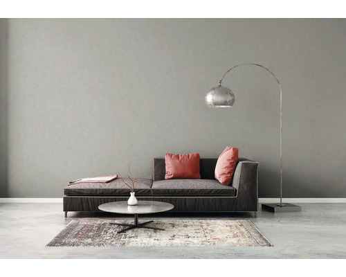 Modernes Wohnzimmer mit dunklem Sofa, rosa Kissen, rundem Steincouchtisch, silberner Bogenlampe und gemustertem Teppich vor grauer Wand.