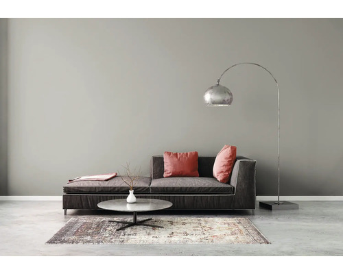 Modernes Wohnzimmer mit grauer Wandfarbe, dunklem Stoffsofa, niedrigem runden Couchtisch, gemustertem Teppich und einer großen Bogenlampe aus Metall.