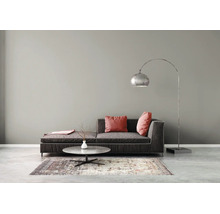 Modernes Wohnzimmer mit dunkelgrauem Sofa, roten Kissen, silberner Bogenstehleuchte, rundem Couchtisch und gemustertem Teppich vor grauer Wand.