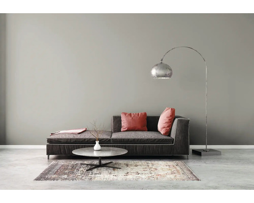 Modernes Wohnzimmer mit dunkelgrauem Sofa, roten Kissen, silberner Bogenstehleuchte, rundem Couchtisch und gemustertem Teppich vor grauer Wand.