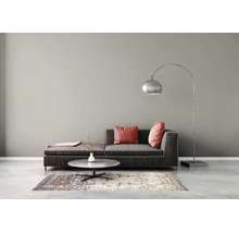 Modernes Wohnzimmer mit grauer Wandfarbe, dunklem Sofa mit roten Kissen, rundem Couchtisch, gemustertem Teppich und einer Bogenstehlampe.