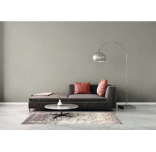 Modernes Wohnzimmer mit strukturierter grauer Wand, dunkelgrauem Sofa, rosa Kissen, Couchtisch und einer großen Bogenlampe aus Metall.
